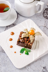 Top view piece of delicious chocolate brownie with nuts and green mint on white plate with of glass cup of tea on gray background. Restaurant kitchen.