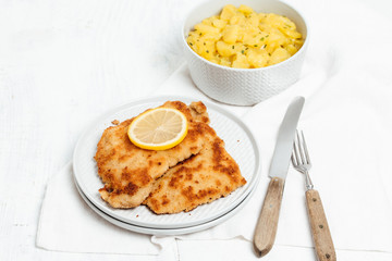 Traditional German or Austrian Wiener Schnitzel or Schnitzel Wiener Art, breaded and pan-fried butterfly cutlet of pork, veal of chicken meat served with slice of lemon and homemade potato salad