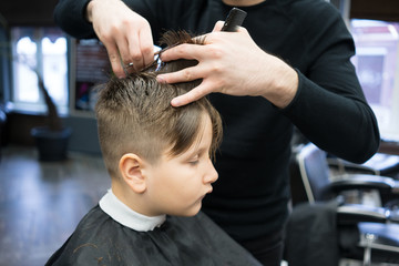Little boy on a haircut in the barber sits on a chair.