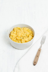 Bowl of traditional German , Austrian or Swiss potato salad made with oil, vinegar and chives, served in light grey bowl on white wooden background