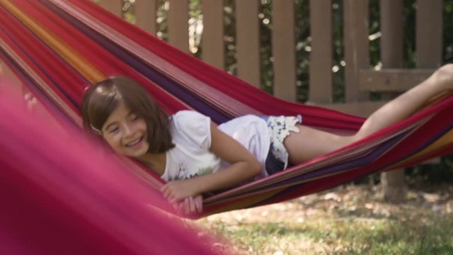 Young happy little girls in summer camp lying in colorful hammocks relaxing playing outside with plushes dog dolls in green grass field kids children slow motion