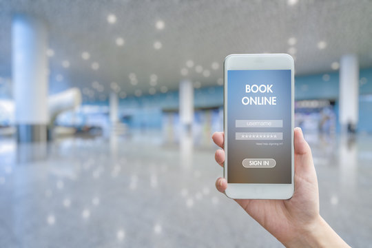 Woman hand holding smartphone against blur bokeh of airport background BOOK online concept - Powered by Adobe