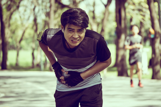 An Asian man has a stomachache while exercising in a park.