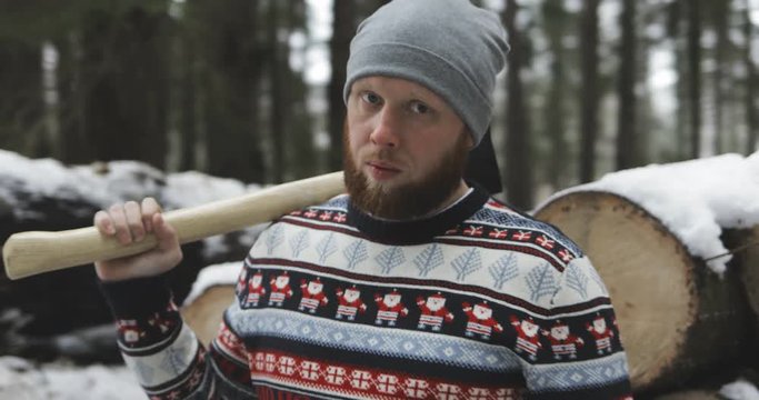 serious brutal bearded man standing near wood, logs, timbers and holding ax (axe, hatchet) in his hands, cold winter weather, forest