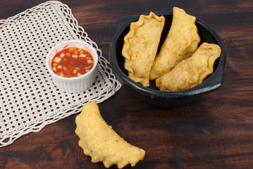 Colombian empanada with spicy sauce on wooden background