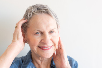 Close up portrait of beautiful older woman with short grey hair and striking blue eyes with hands near face against neutral background (selective focus)