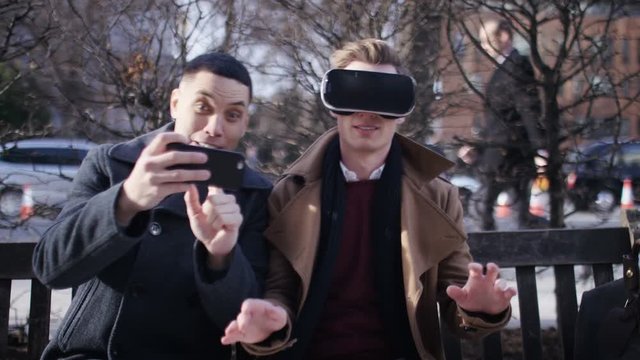 Two young men on a bench syncing their phone and virtual reality headset