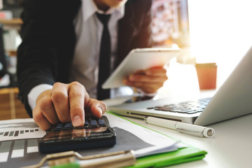 businessman hand working with finances about cost and calculator and laptop with tablet on withe desk at office in morning light
