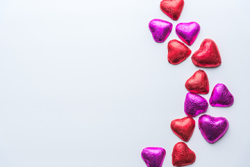 Red and pink foil wrapped heart shaped chocolates scattered across right side of white background