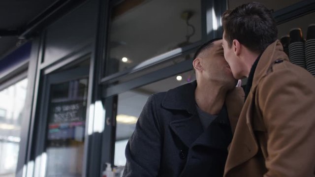 Young adult male couple star a kiss outside a coffee bar, in slow motion 