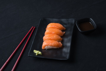 Salmon sushi on black plate with soy sauce