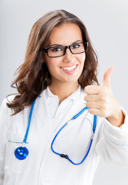 Female doctor with thumbs up gesture, over grey
