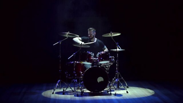 Male drummer playing drums on a black background, slow motion. A man playing drums at a concert or party. Empty stage and concert lighting with smoke.