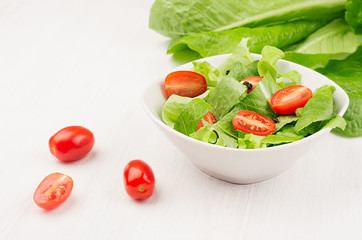 Spring fresh salad of green spinach and cherry tomato slices in white bowl on white wood background, closeup, copy space.