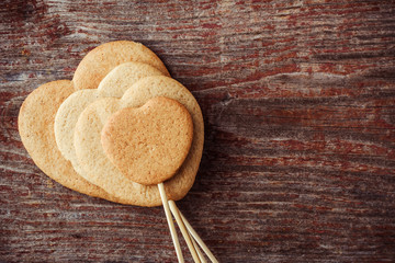 Ginger cookies on a stick in the form of hearts on a wooden background. Top view