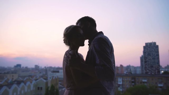 Handsome man gently kissing his girl warming her from evening coolness, sunset