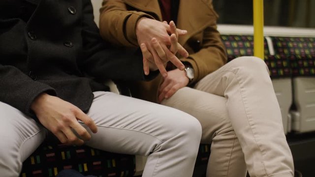Young same sex male couple hold hands on a subway train, in slow motion 