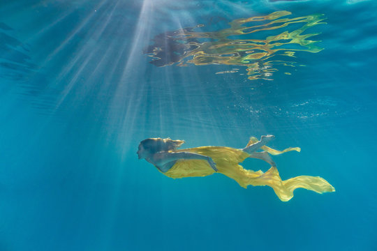 underwater picture of attractive young woman in dress swimming in swimming pool
