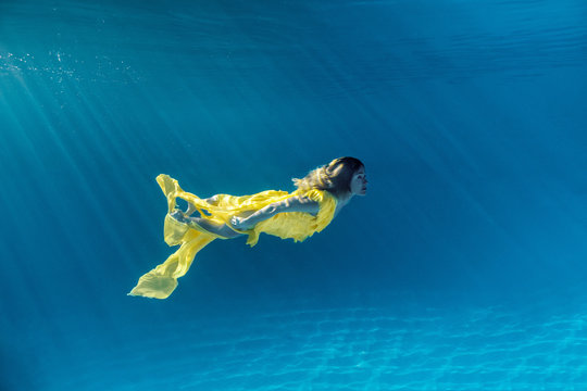 underwater picture of beautiful young woman in dress swimming in swimming pool