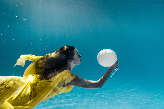 underwater picture of beautiful young woman in dress with balloon swimming in swimming pool