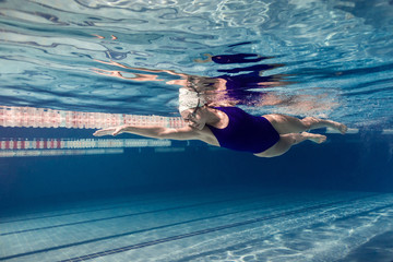 underwater picture of female swimmer in swimming suit and goggles training in swimming pool