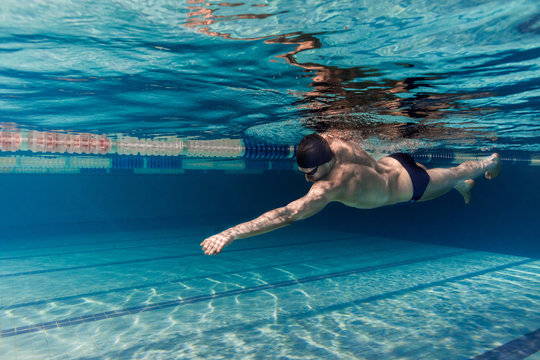 underwater picture of young swimmer in cap and goggles training in swimming pool