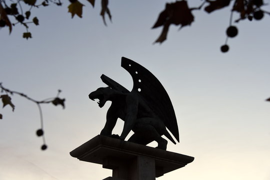 Mystische Skulptur eines L&ouml;wen mit Fl&uuml;geln auf der Puente del Regn umrahmt von Zweigen