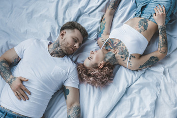 top view of tattooed couple looking at each other and lying on bed