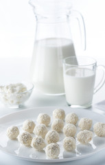 Coconut candies on a background of a jug and a cup of milk and bowls of cottage cheese
