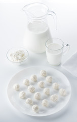 Coconut candies on a background of a jug and a cup of milk and bowls of cottage cheese