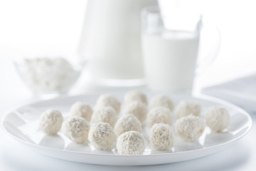 Fototapeta na wymiar Coconut candies on a background of a jug and a cup of milk and bowls of cottage cheese