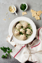 Homemade chicken matzo ball soup with parsley and garlic in simple white ceramic plate on a gray stone or concrete background.  Traditional Jewish passover dish. Selective focus. Top view.
