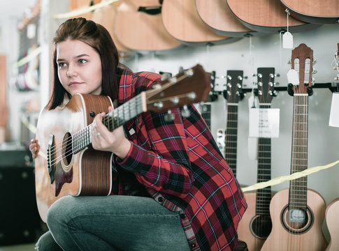Smiling teen girl examining various acoustic guitars