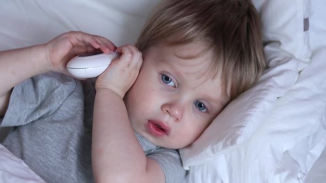 Measuring baby's temperature with contactless digital infrared thermometer in the ear. 2 years old kid measures its temperature in the ear himself