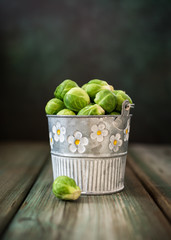 Fresh Brussels sprouts in metal bucket on old wooden table. Healthy food concept with copy space.