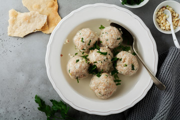 Homemade chicken matzo ball soup with parsley and garlic in simple white ceramic plate on a gray stone or concrete background.  Traditional Jewish passover dish. Selective focus. Top view.