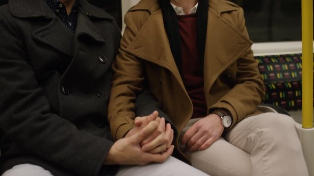 Young male couple on a subway train holding hands as they talk