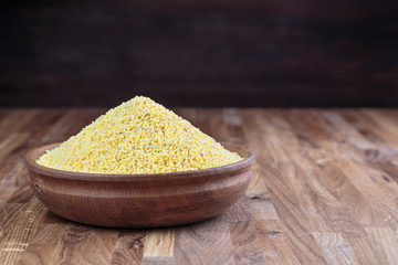 Millet in a wooden bowl standing on the kitchen table made of oak. 