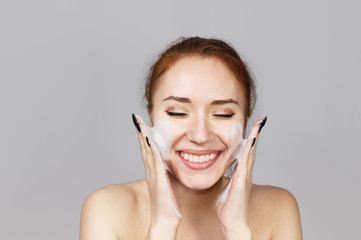 Red-haired girl in foam for washing isolated on gray.