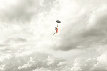 Surreal moment of an elegant woman flying in the middle of the clouds hanging on her umbrella