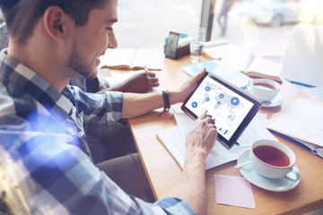 Do analysis. Profile photo of positive bearded man holding tablet in his hands and looking at his gadget while doing task