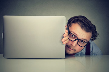 Modest young man hiding behind laptop