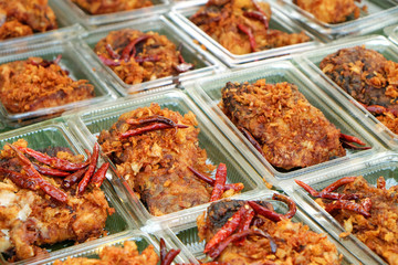 Many pieces of deep fried fish with the garlic and red chili in plastic boxes