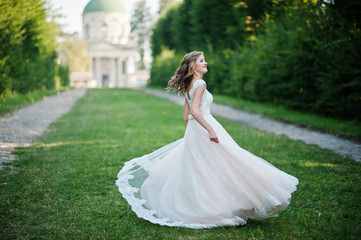 Fototapeta premium Lonely attractive bride walking on the green alley which leads to a church.