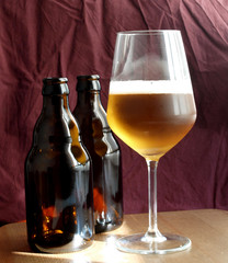two brown glass beer botles and one glass of fresh beer over dark fabric background