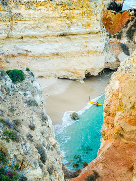 Tiny Remote Beach In Lagos, Algarve, Portugal. A Hidden Secret Beach Between Limestone Walls. People With A Yellow Kayak Visiting The Beach.