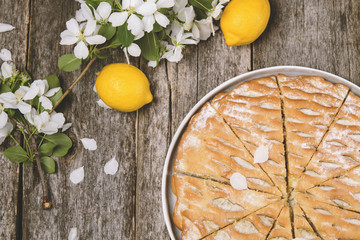 Lemon apple pie, cake sliced on vintage rustic wooden table, decorated flowering branches apple tree. Top view. Soft sunny toning. Selective focus 