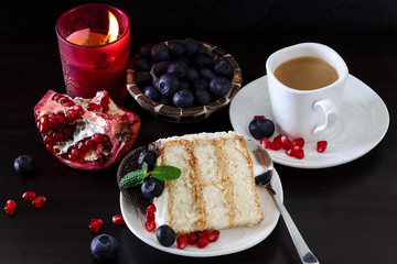 Still life Piece of layer cake with blueberries, chocolate cookies and pomegranate. Dark wooden background. Burning candle. Romantic Valentine's Day concept. Selective focus.