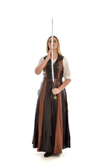 full length portrait of girl wearing brown  fantasy costume, holding a sword. standing pose on white studio background. 