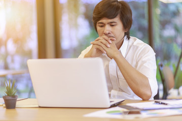 Hard think on the analysis in the work. Asian business man is working on laptop computer. Freelance male working at office with laptop and documents on his desk. Analyze plans